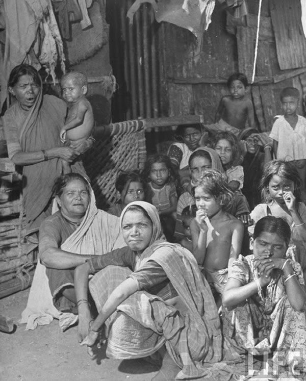 Indian women & children sitting in the alley between shacks in the Chawls