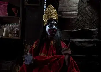 Performer in Kali costume with gold crown, face paint, holding an ID card