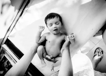 Newborn baby being held up with arms outstretched, black and white photo