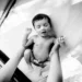 Newborn baby being held up with arms outstretched, black and white photo