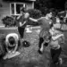 Family in a cluttered yard, child running while woman writes on cardboard, black and white photo