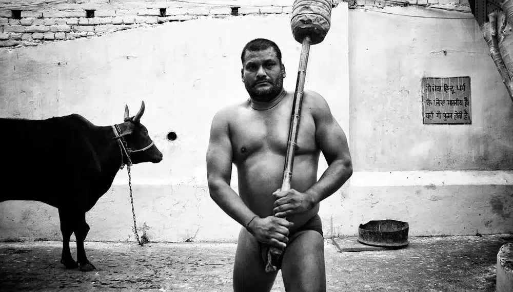 Indian kushti wrestler holding a traditional mace beside a bull, black and white photo