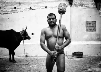 Indian kushti wrestler holding a traditional mace beside a bull, black and white photo