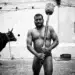 Indian kushti wrestler holding a traditional mace beside a bull, black and white photo