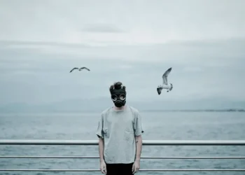 Man in a gas mask standing by the sea with seagulls, fine art photography