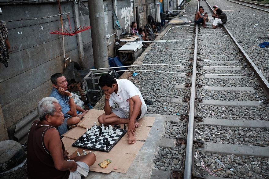 Men Are Playing Chess Next To The Active Railway Tracks. Trains Pass By Approximately Every 10-20 Minutes