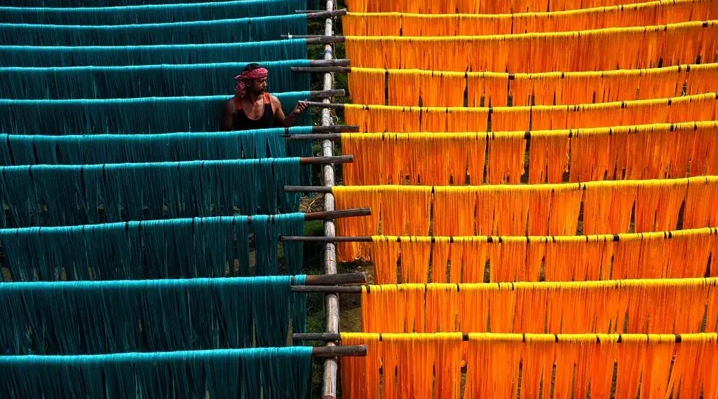 Worker tending vibrant teal and orange dyed yarn hanging to dry on wooden racks