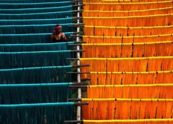 Worker tending vibrant teal and orange dyed yarn hanging to dry on wooden racks