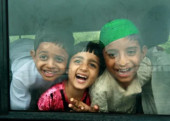 Three laughing children looking through a bus window with joyful expressions