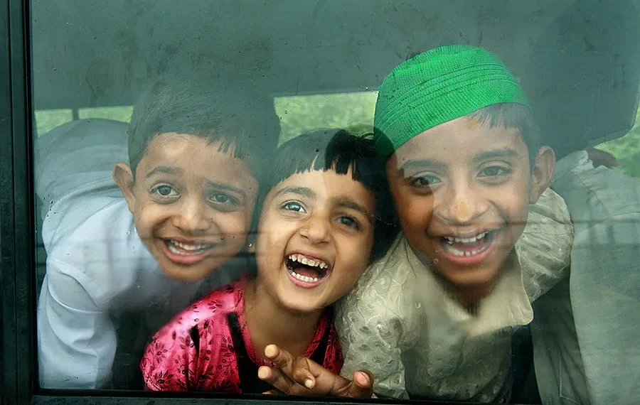 Three laughing children looking through a bus window with joyful expressions