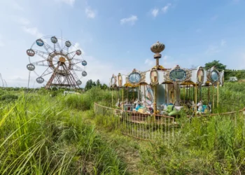 Abandoned carousel and ferris wheel overgrown with weeds in Japan