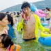 Man on phone in neon jacket amid crowded beach swimmers with colorful floats