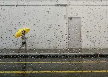 Famous street photographers capturing a person with yellow umbrella through a rain-covered window