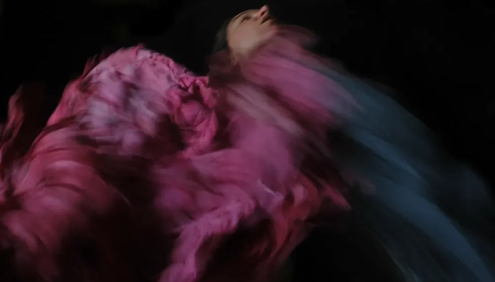 Woman spinning in a flowing pink dress, motion blur against dark background
