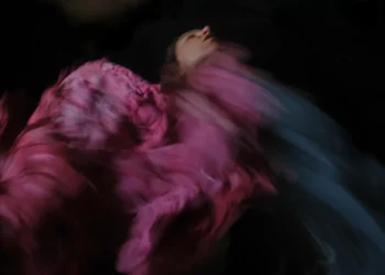 Woman spinning in a flowing pink dress, motion blur against dark background