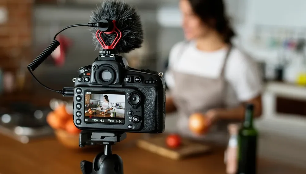 SLR camera on tripod filming woman cooking in kitchen