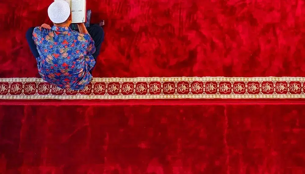Man reading Quran on red mosque carpet, red color photography