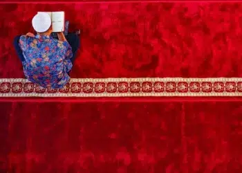 Man reading Quran on red mosque carpet, red color photography