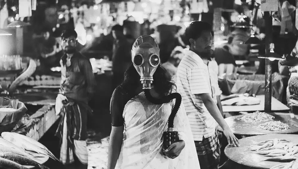 Woman in saree wearing gas mask stands in a busy fish market