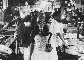 Woman in saree wearing gas mask stands in a busy fish market