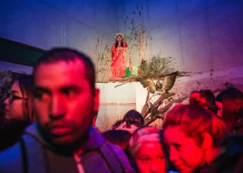 Crowd watching a woman in red sitting on a staged installation indoors