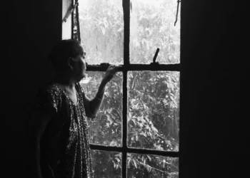Elderly woman gazing through a rain-streaked window, black and white