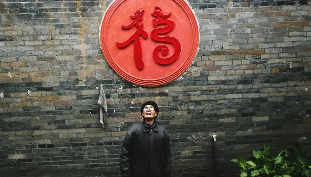 Candid Photography - How to Shoot Excellent Candids 1 Man looking up beneath red Chinese symbol on brick wall candid photo