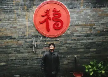 Man looking up beneath red Chinese symbol on brick wall candid photo