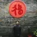 Man looking up beneath red Chinese symbol on brick wall candid photo