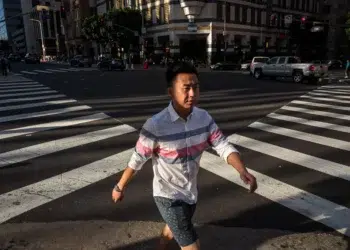 Man walking across sunlit city crosswalk at intersection