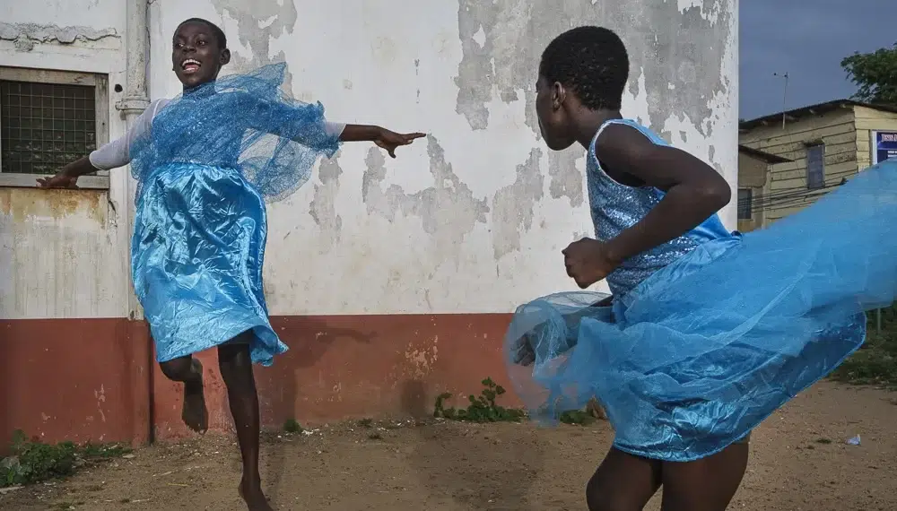 Two girls dancing joyfully in blue dresses outside a weathered wall