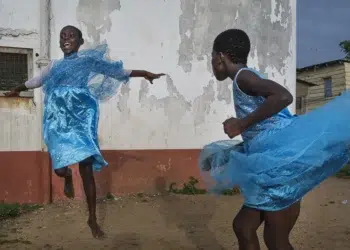 Two girls dancing joyfully in blue dresses outside a weathered wall