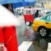 Woman in a red coat with a blue umbrella crossing a rainy city street