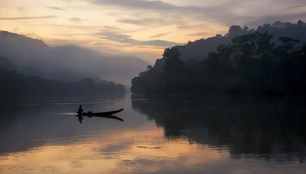 Lone fisherman in a canoe on a misty river at dawn