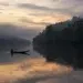 Lone fisherman in a canoe on a misty river at dawn