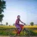 What is An Environmental Portrait - Tips & Examples 23 Smiling girl on an orange bicycle beside green fields in a rural setting