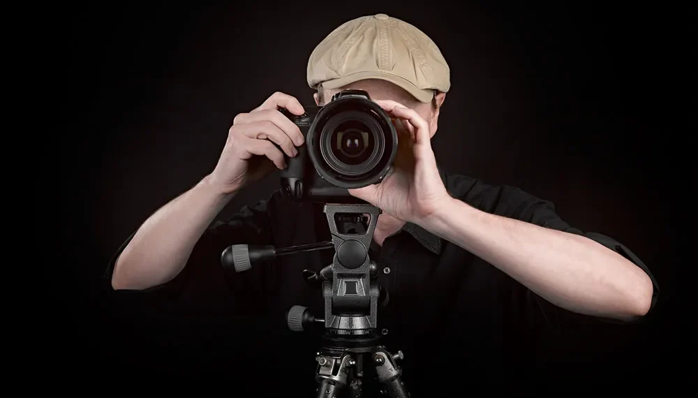 Photographer taking a photo with DSLR camera on tripod against dark background