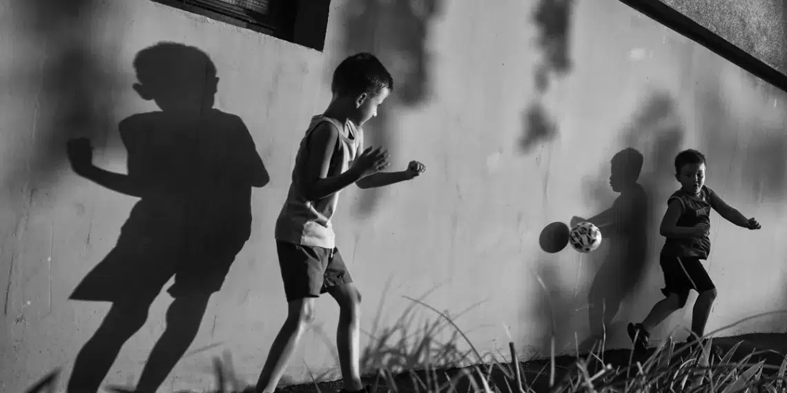 Street photographer captures two boys playing football against a wall with dramatic shadows