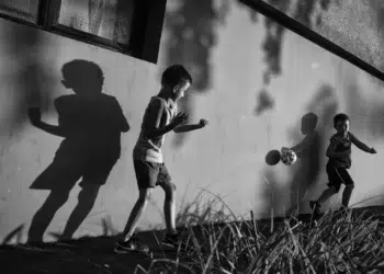 Street photographer captures two boys playing football against a wall with dramatic shadows