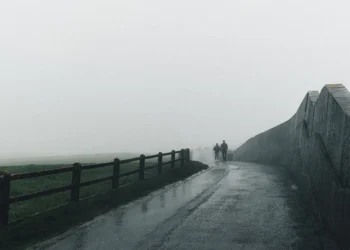 Two figures walking a misty coastal path beside a stone wall, Ireland