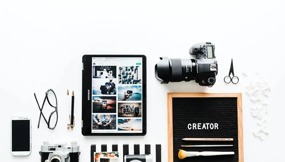 Flatlay of cameras, tablet, phone, and a letter board reading "CREATOR"