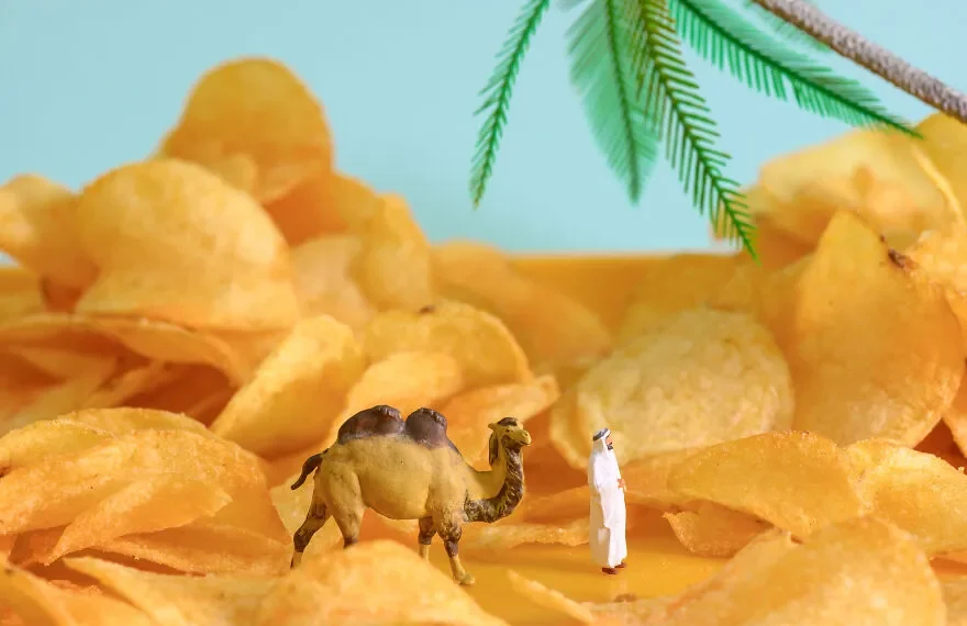 Miniature camel and figure standing among potato chips styled as a desert scene