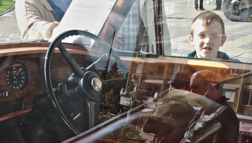 Boy peering into a vintage car window, candid street photography
