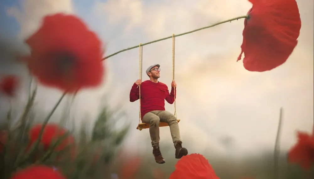 Man swinging from a giant poppy stem in a surreal flower field