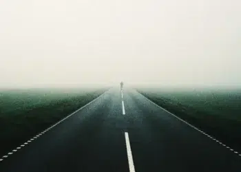 Person walking alone on a foggy road through open landscape