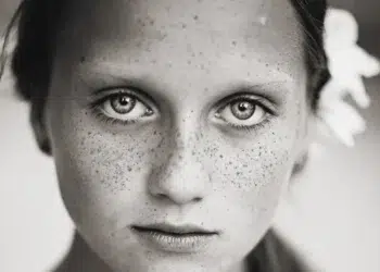 Close-up black and white portrait of a freckled girl with intense eyes