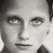 Close-up black and white portrait of a freckled girl with intense eyes