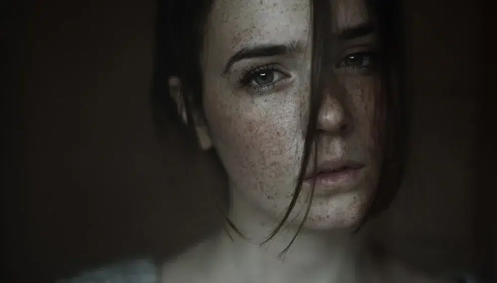 Moody close-up portrait of a freckled woman with hair across her face