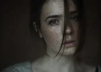 Moody close-up portrait of a freckled woman with hair across her face