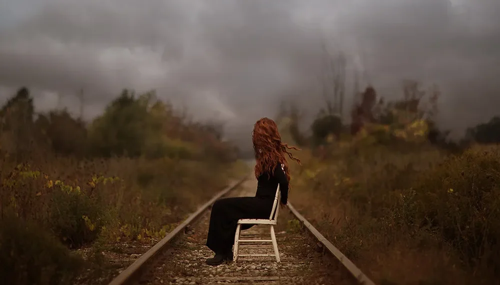 Patty Maher photography of a red-haired woman sitting on a chair on railway tracks